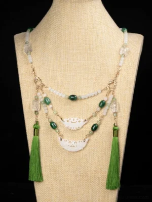 Front close-up of a layered Warring States style Chinese necklace with green and pale white beads, gold-tone hardware, carved white pendants, and long green silk tassels on a linen mannequin