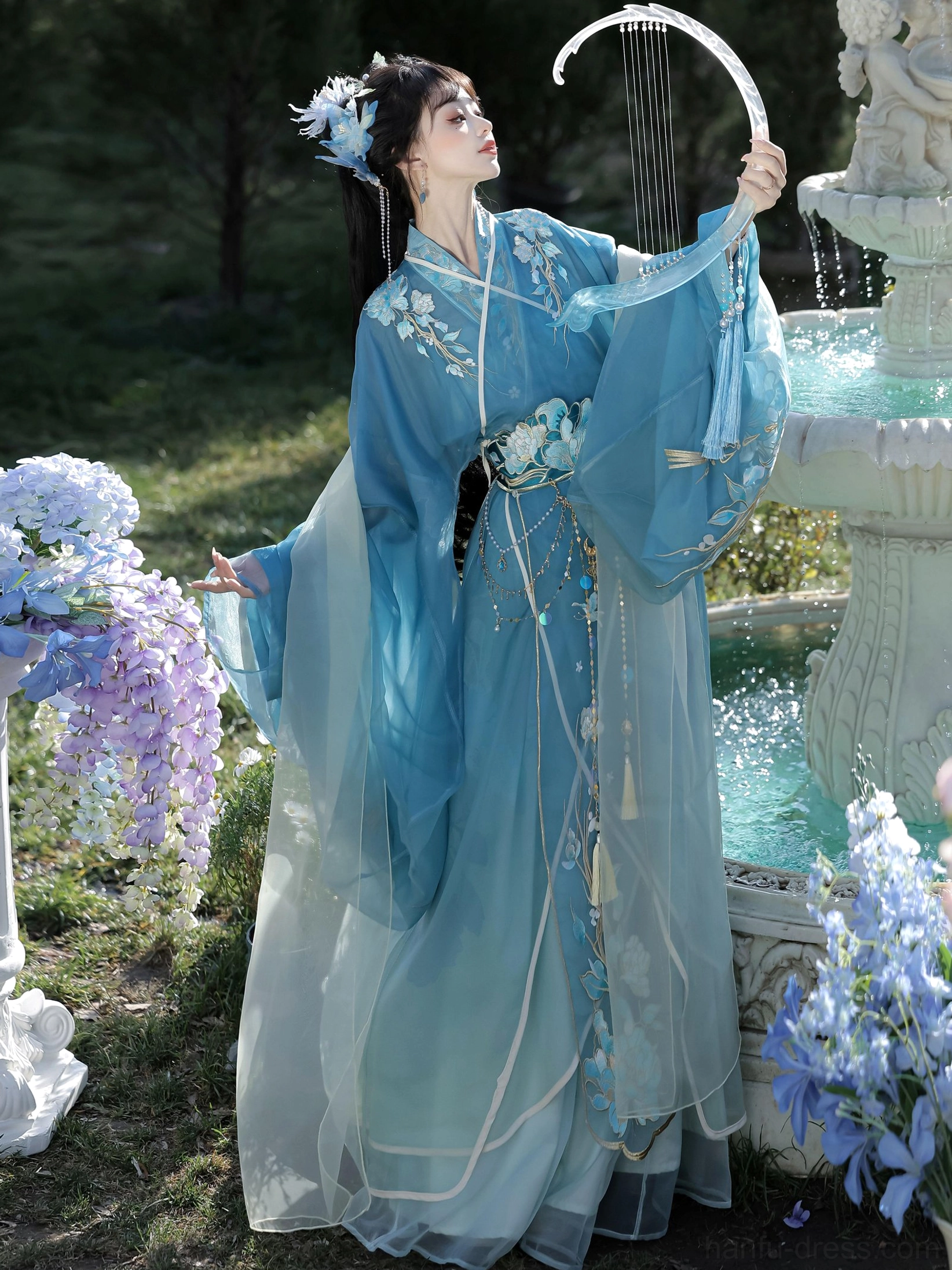 Warring States and Han Dynasty-inspired blue Hanfu robe shown from the side with embroidered flowers, flowing gradient fabric, tassel belt, and ancient harp styling
