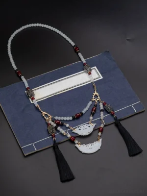 Full flat lay of Warring States inspired Chinese yingluo necklace with layered chains pearls red agate beads and black tassels on a traditional book