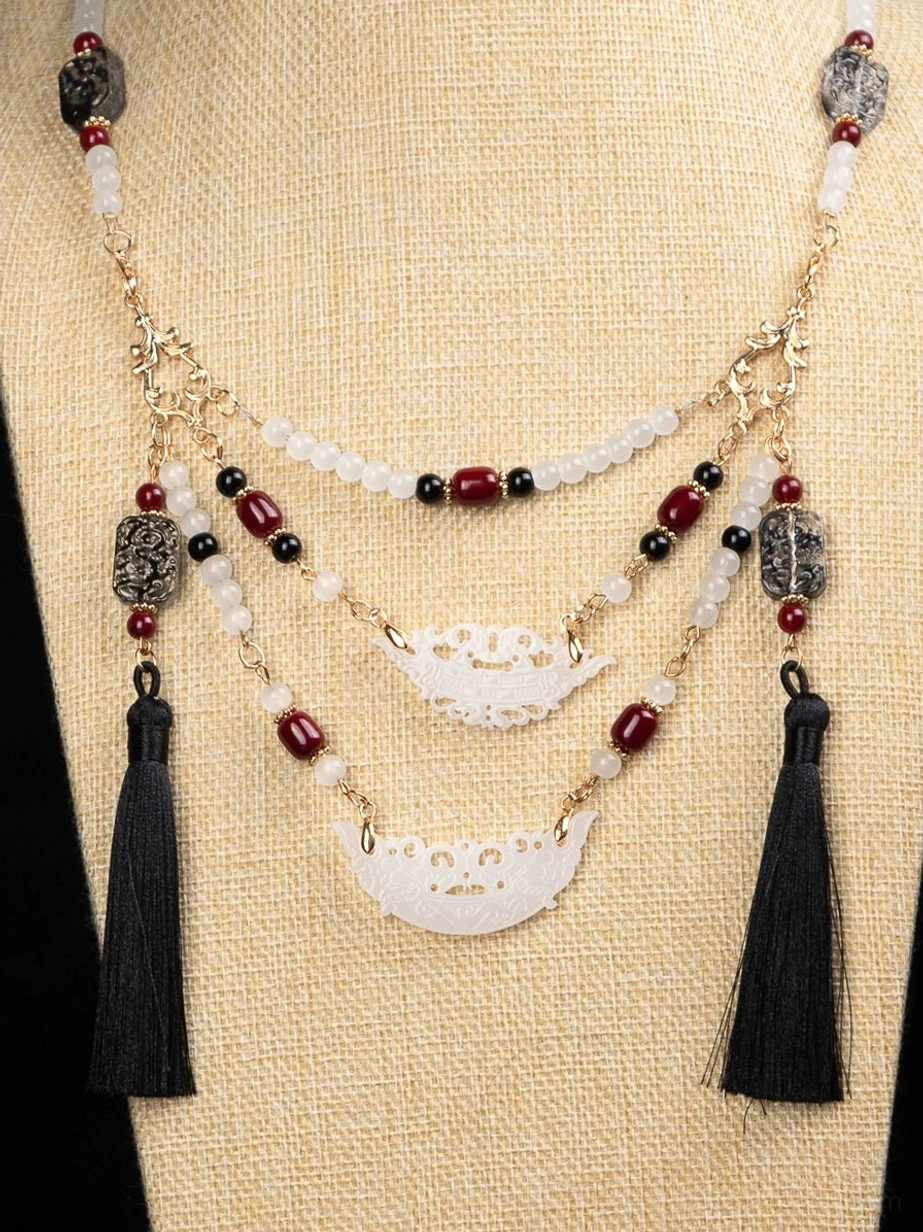 Warring States style multilayer Chinese necklace flat lay showing carved white semi-circular pendants burgundy beads gold tone chains and black tassels