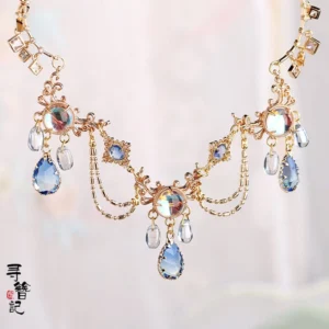 Water Fairy blue teardrop Chinese necklace for Hanfu displayed on light pink fabric with gold tone floral details and pearl accents