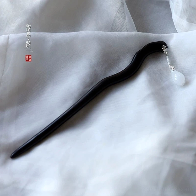 Wavy ebony Chinese hair stick displayed on soft white fabric with a sleek black wooden shaft, silver chain, and teardrop white jade pendant