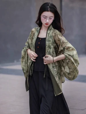 Front three quarter view of a woman wearing an olive green Wei Jin style bamboo print modern Hanfu cardigan with flowing oversized sleeves dark green lapel trim and waist ties