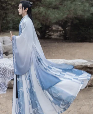 Side profile of male model in flowing blue and ivory Wei Jin hanfu for men featuring wide sleeves, abstract printed skirt, black waist ties, and folding fan