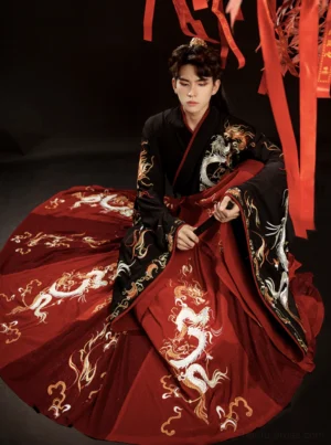 Front seated view of a male groom in a dramatic wine red Chinese wedding Hanfu with black cross-collar trim, wide sleeves, white dragon embroidery, and traditional Wei Jin style ceremonial details