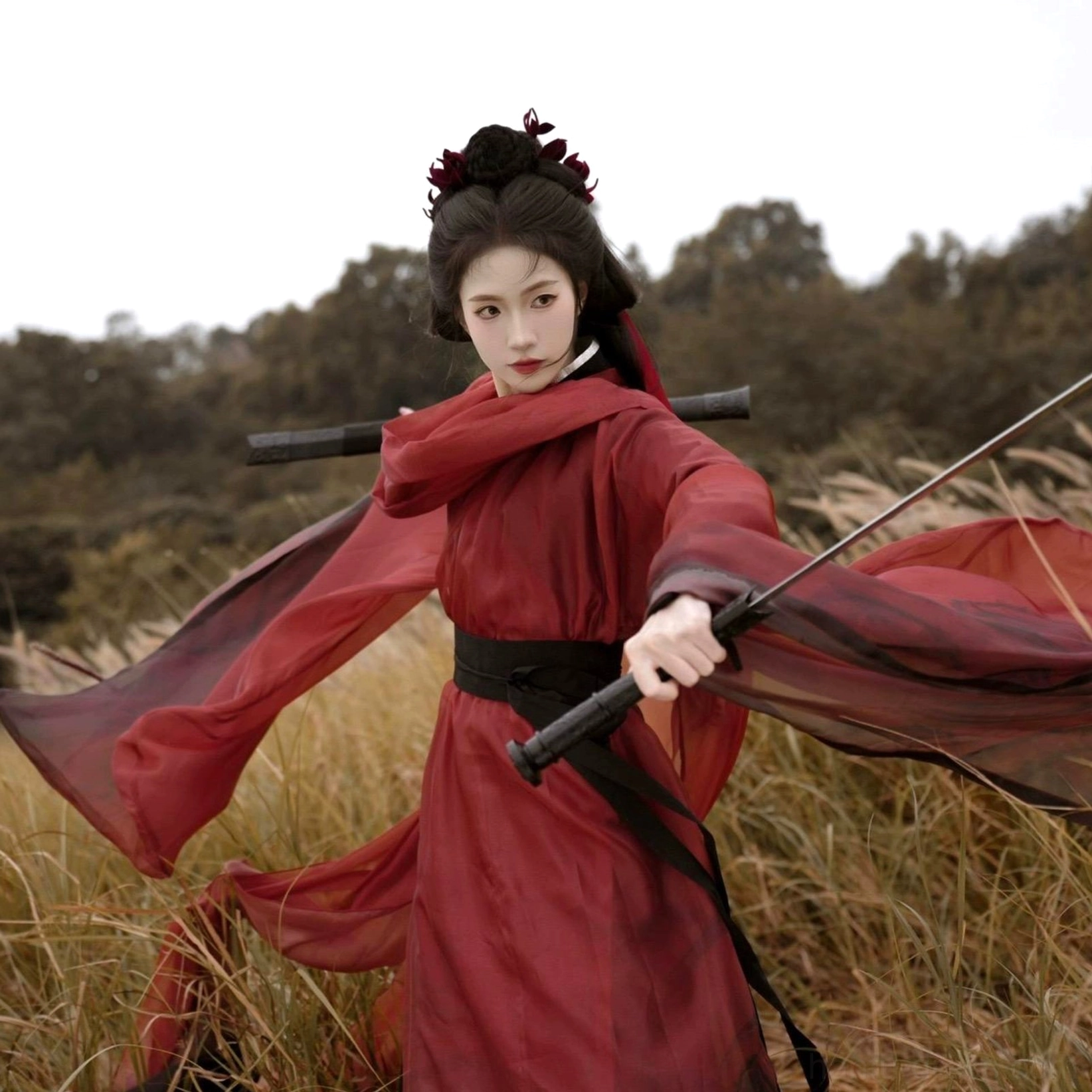 Distant action view of a red Wei Jin Dynasty chivalry Hanfu with black belt, trimmed cross collar, flowing sheer robe, and swords sheathed on the back