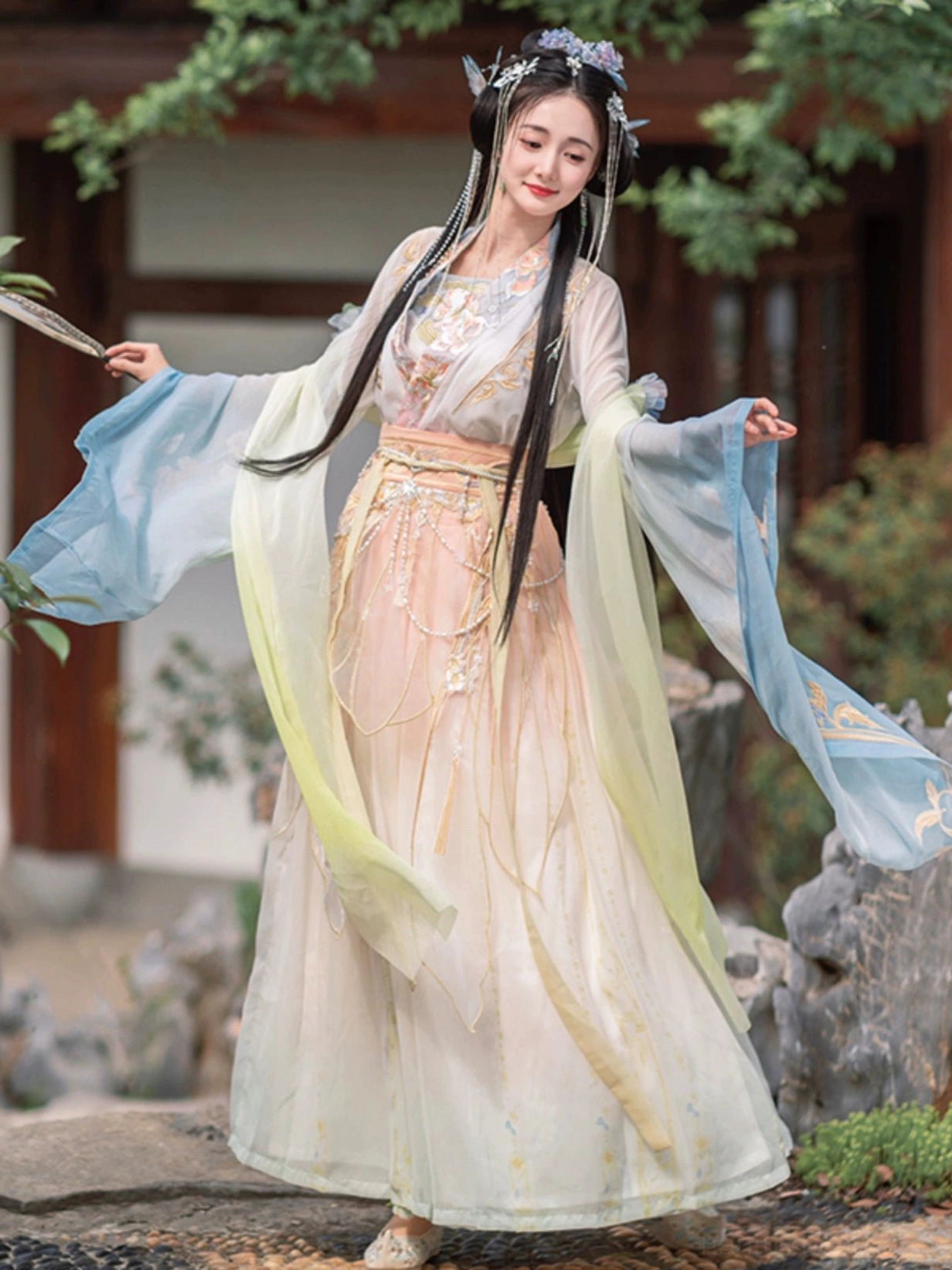 Back three-quarter view of a flowing Wei Jin Dynasty Hanfu with blue-green gradient sleeves, floral embroidery, wide waistband, and full skirt in a traditional Chinese courtyard