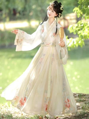 Side three-quarter view of an ethereal Wei Jin Dynasty Hanfu with ivory cross-collar top, floor-length skirt, wide flowing sleeves and floral hem beside a lakeside garden