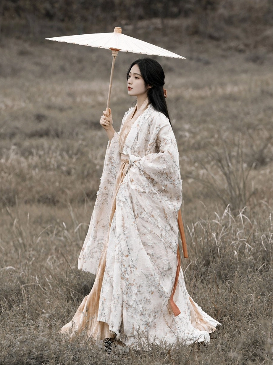 Side profile of a woman in Wei Jin Dynasty Hanfu featuring a flowing floral robe floor-length beige dress and orange decorative waist sash