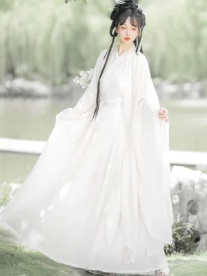 Side view of an ivory Wei Jin Dynasty Hanfu dress with oversized sleeves, pleated high-waist wrap skirt, and flower bouquet beside a lakeside garden