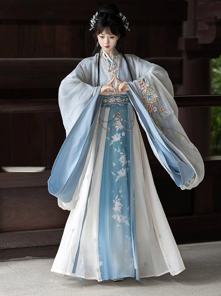 Blue and white gradient Wei Jin Dynasty Qiyao Ruqun Hanfu full front view with floral details, wide sleeves, cross-collar top, and flowing wrap skirt in a traditional Chinese courtyard