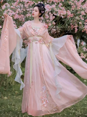 Pastel pink gradient Wei Jin Dynasty Qiyao Ruqun Hanfu with floral embroidery, flowing ruffled sleeves, beaded waist detail, and long skirt modeled in a flower garden