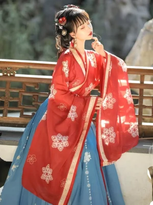 Wei Jin Dynasty Qiyao Ruqun Hanfu three quarter seated view showing red embroidered upper robe, blue pleated skirt, gold sleeve trim, and elegant flowing sleeves