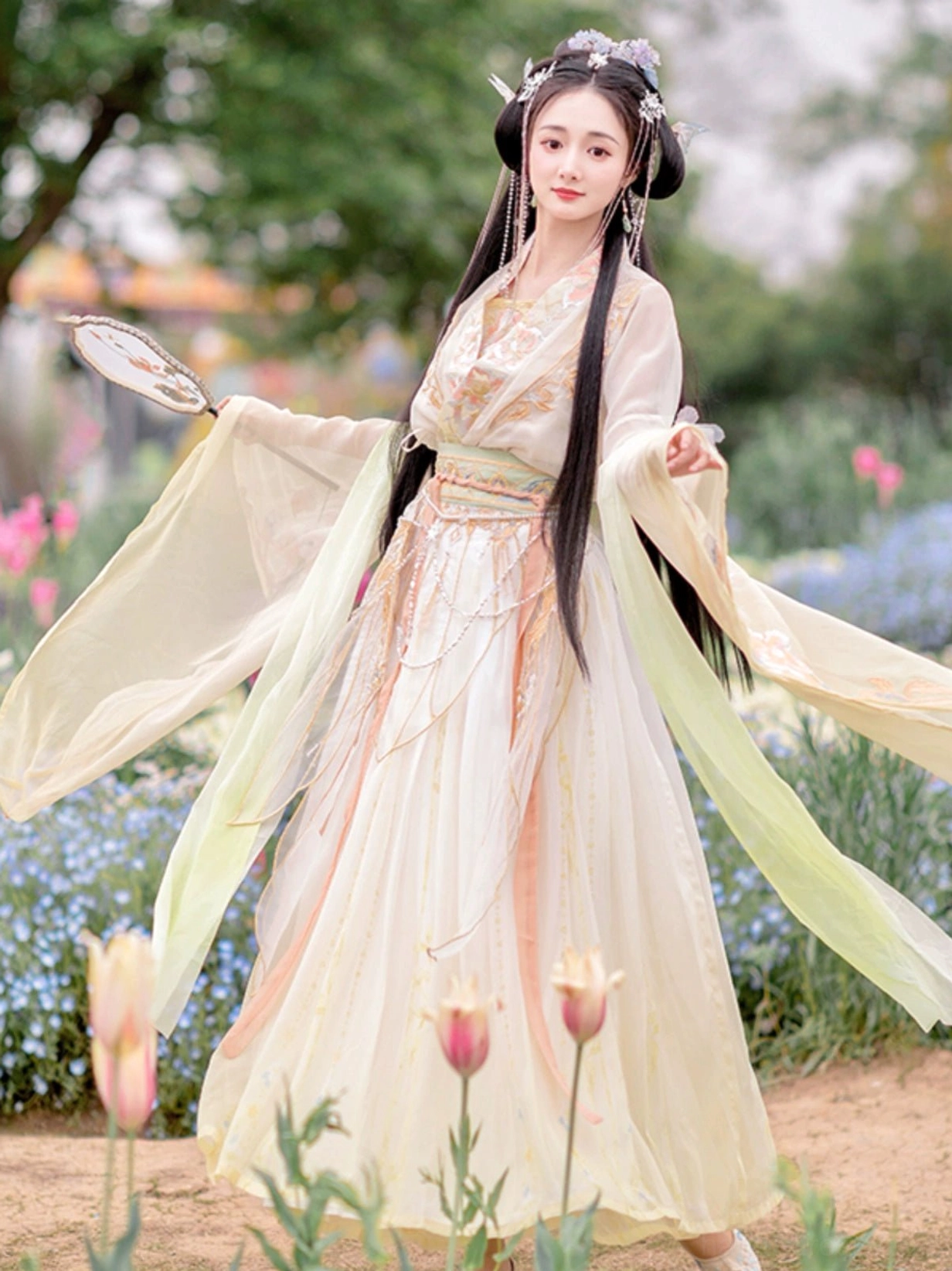 Side view of a Wei Jin Dynasty Qiyao Ruqun Hanfu with a cross-collar top, apricot to ivory gradient skirt, traditional hair ornaments, and folding fan in a flower garden