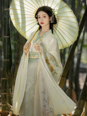 Full-body front view of a cream and sage green Wei Jin Dynasty Qiyao Ruqun Hanfu with floral embroidery, wide flowing sleeves, traditional cross collar, and long wrap skirt in a bamboo forest