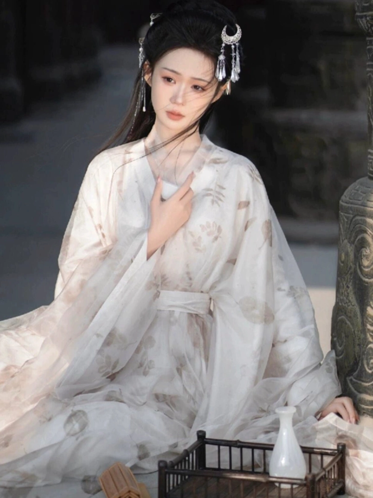 Full-body seated view of a woman in flowing Wei Jin Dynasty Qiyao Ruqun Hanfu with a long sheer skirt, oversized silhouette and dried-flower print beside a traditional tea setting