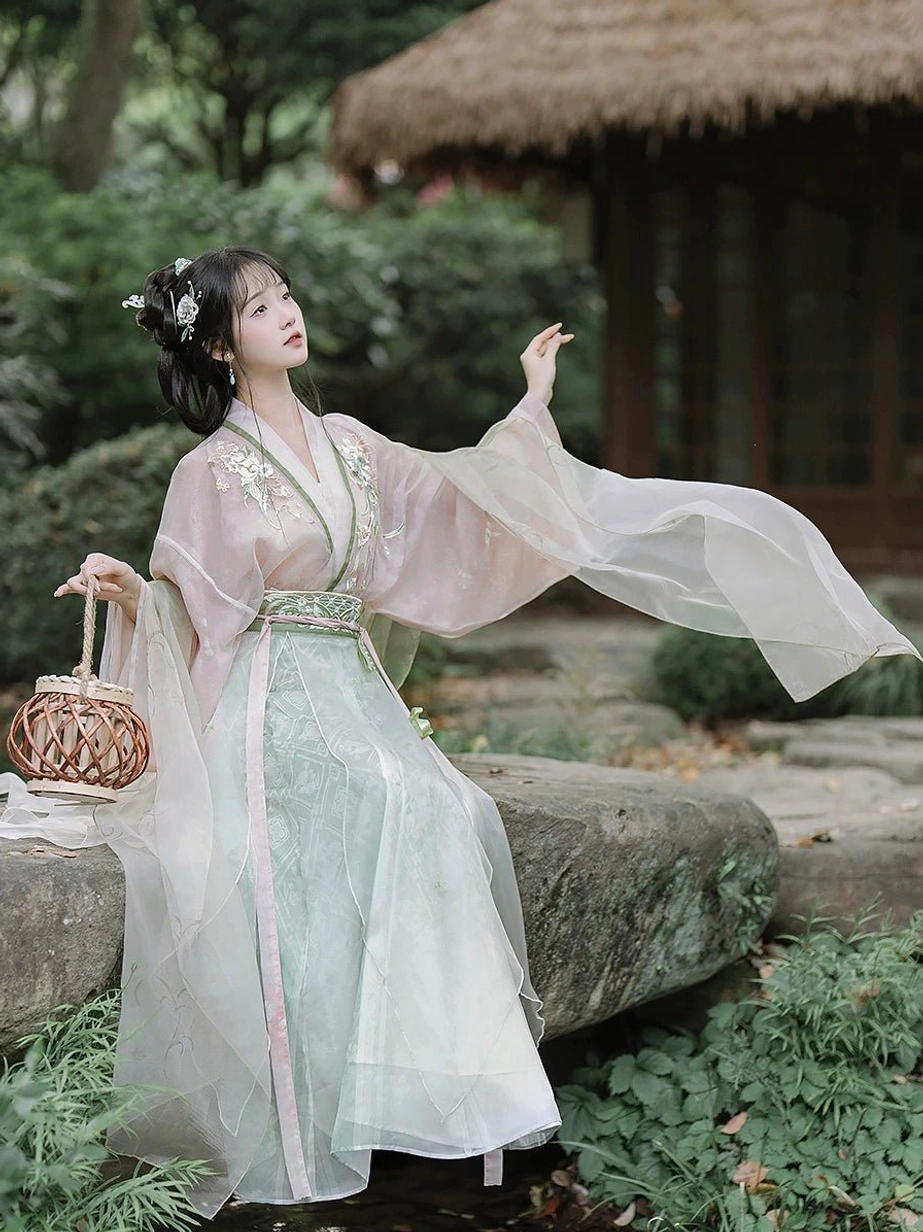 Side view of an ethereal Wei Jin Qiyao Ruqun Hanfu with flowing translucent robes, pine green waist details, floral hair accessories, and pastel skirt in a lush Chinese garden