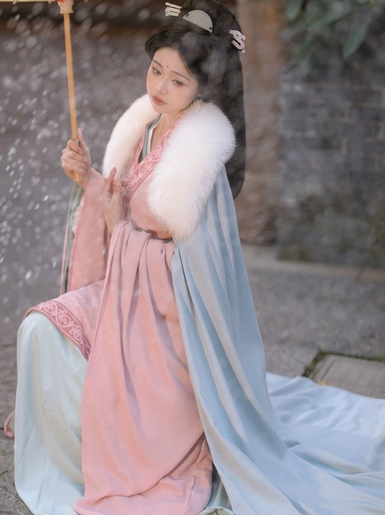 Wei Jin style Hanfu set with pink top light blue floor-length skirt embroidered trims and white fur-trimmed cloak shown in a seated three-quarter view