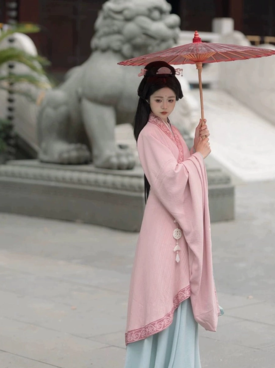Wei Jin style Hanfu pink cross-collar top and light blue long skirt with embroidered trims shown beside a traditional Chinese stone lion