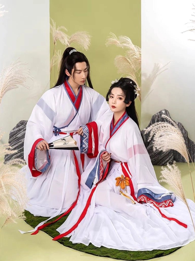Seated Wei Jin xianxia hanfu couple in coordinated white traditional Chinese outfits with red sashes, flowing pleated skirt, and wuxia-inspired fan styling