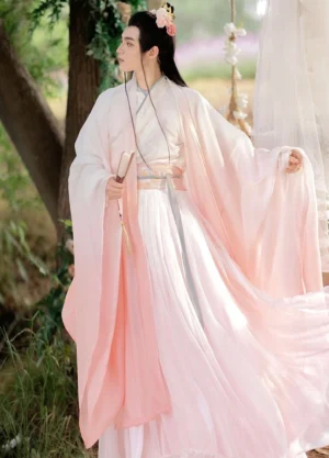 Front three-quarter view of male Wei Jin xianxia hanfu in layered white and pink gradient robes with cross-collar top and pleated skirt in a woodland setting