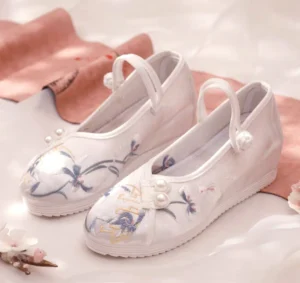 Pair of white embroidered Chinese Hanfu shoes for women with blue floral and crane embroidery, golden traditional motifs, pearl decorations, Chinese knot ankle straps, and low wedge rubber soles