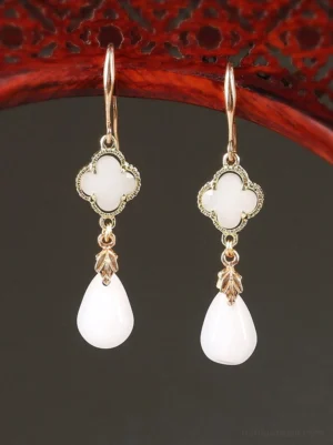 White four leaf clover drop Chinese earrings with vintage gold tone frames and teardrop pendants displayed on a red carved wooden decorative rack