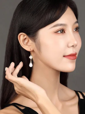 Model wearing elegant white four leaf clover drop earrings with teardrop pendants styled against a simple grey background