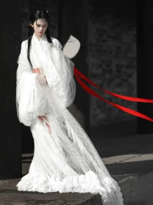 White Warring States and Han Dynasty inspired Hanfu robe with floral lace fabric wide flowing sleeves red ribbons and dramatic trailing train shown in an ancient Chinese courtyard