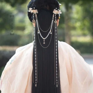 White hibiscus Hanfu back hair pin worn with a traditional Chinese hairstyle, featuring gold-tone details, pearl strands and long layered chain tassels in a garden setting