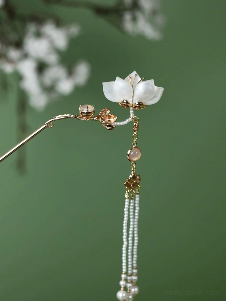 White lotus Chinese hair pin with gold tone stick brown accent bead and layered pearl tassels on green floral background