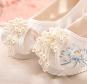 Close-up of white traditional Chinese Hanfu shoes with blue lotus embroidery, pearl clusters, tassels, and canvas upper