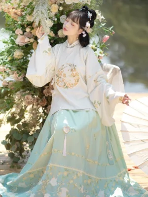 Three-quarter seated view of a white Ming Dynasty hanfu top with round floral embroidery and gradient blue rabbit print mamianqun skirt beside flowers