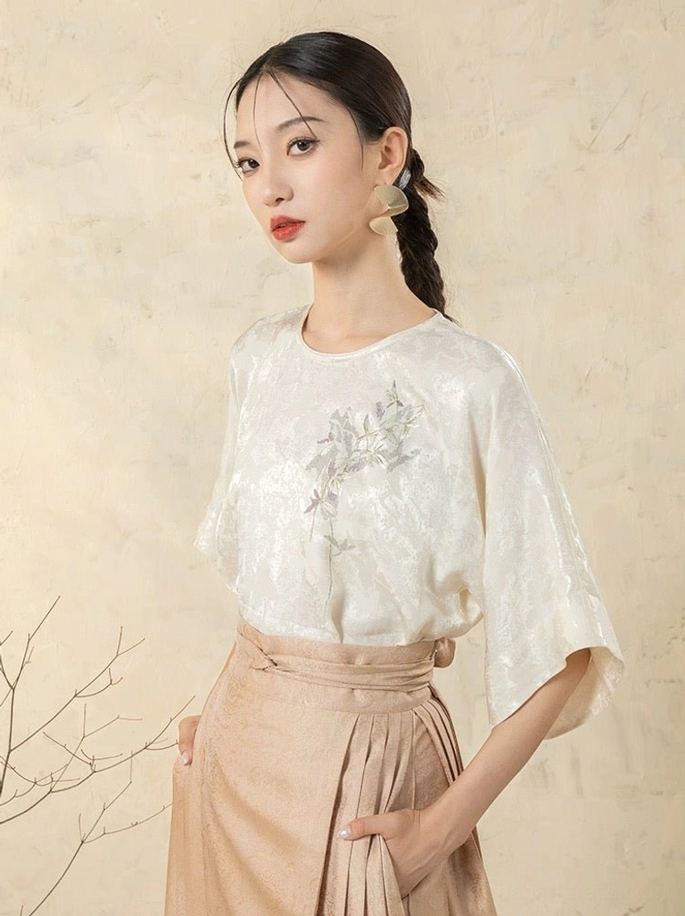 White satin modern Hanfu top with subtle jacquard texture, embroidered botanical chest detail, round neckline, dolman sleeves, and khaki horse-face skirt