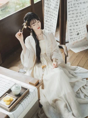 White Moonlight cream Song Dynasty Qiyao Ruqun Hanfu worn by a woman seated in a traditional Chinese study with calligraphy scrolls, tea set, wide sheer sleeves, pleated skirt, tassel waist pendant, and delicate hair ornaments
