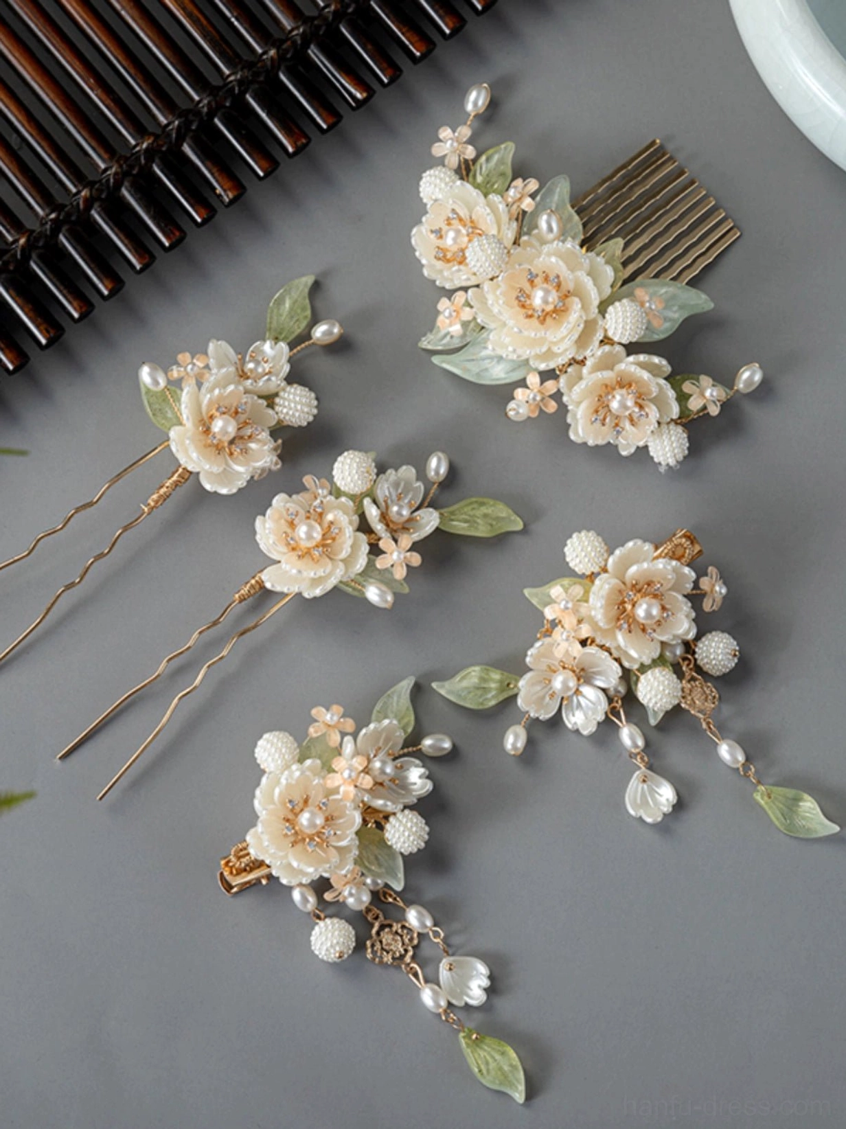 White peony Hanfu hair accessories set flat lay with floral hair comb, pearl tassel clips, U-shaped hairpins, green leaves, and gold-tone details