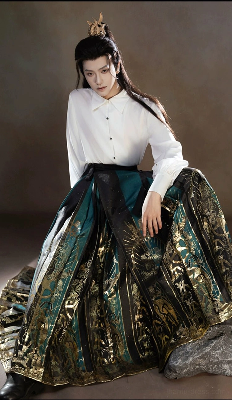 Side seated view of a white stand collar shirt paired with a high waisted Sanxingdui patterned mamianqun horse face skirt in dark green and gold