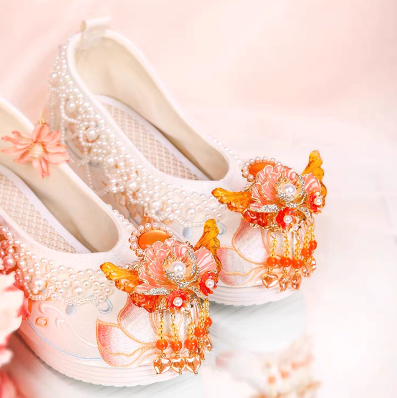 Close-up of white traditional Chinese wedge heel Hanfu shoes with orange-red floral tassels, butterfly decorations, pearl edging, and lotus embroidery