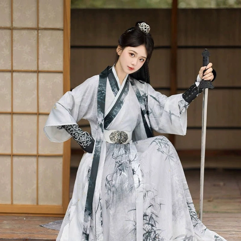 Low-angle view of a white Wei Jin Dynasty Qiyao Ruqun Hanfu with dark green-trimmed cross collar, ink bamboo printed long skirt, embroidered arm guards, and decorative metal belt