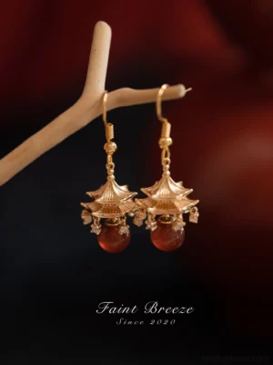 Front close-up of gold tone wind chime pavilion Chinese drop earrings with red agate-style bead pendants and sparkling details for Hanfu jewelry styling