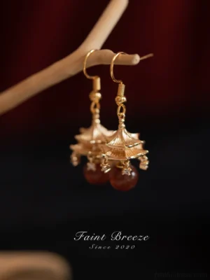 Side view of traditional Chinese pavilion Hanfu earrings showing layered pagoda charm, gold hook closure, and dangling red stone bead