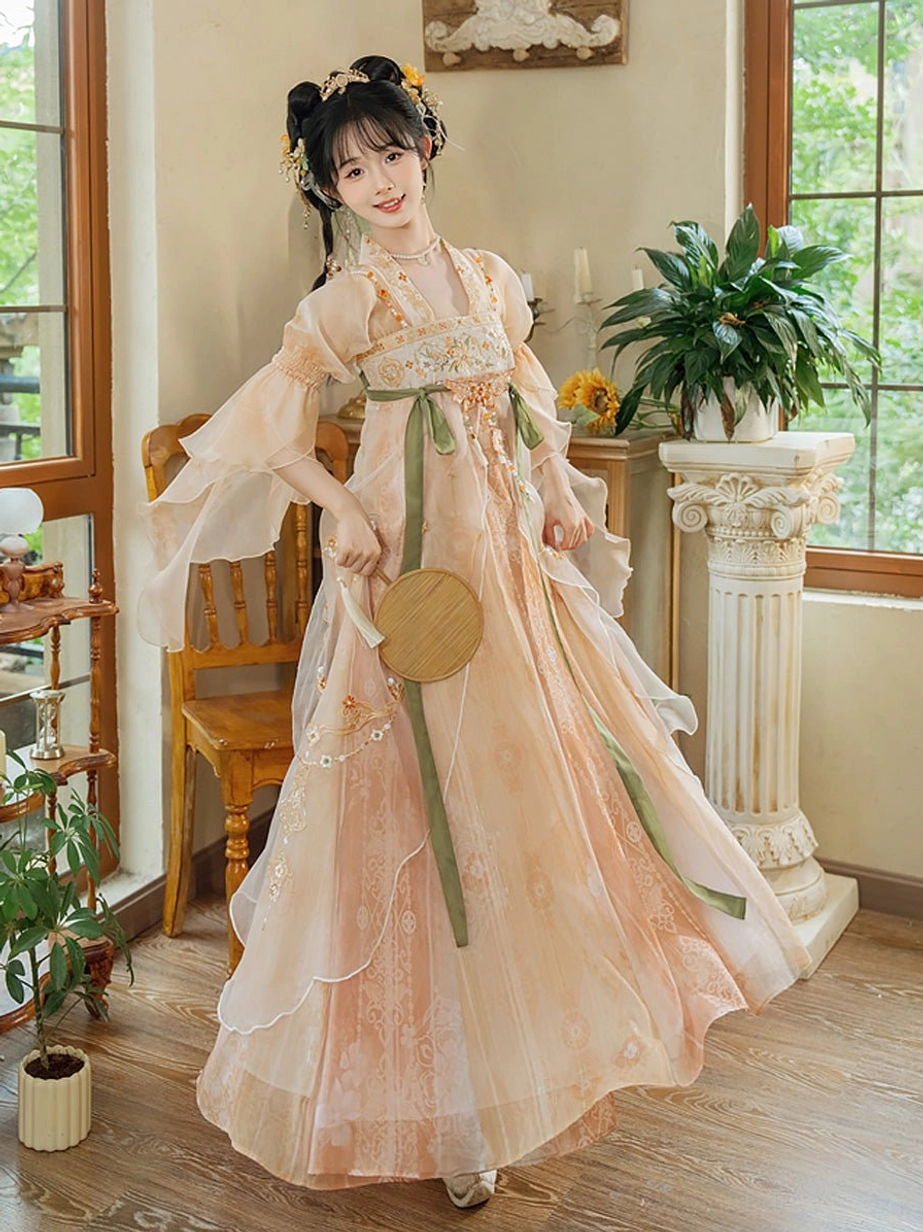 Traditional Tang style Hanfu dress with apricot pink sheer fabric, floral embroidered skirt, green waist sashes, flutter sleeves, and wooden fan styling