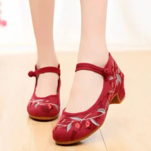 Wine red embroidered Hanfu shoes worn on feet, featuring floral leaf embroidery, Chinese knot ankle straps, low block heels, canvas uppers and rubber soles