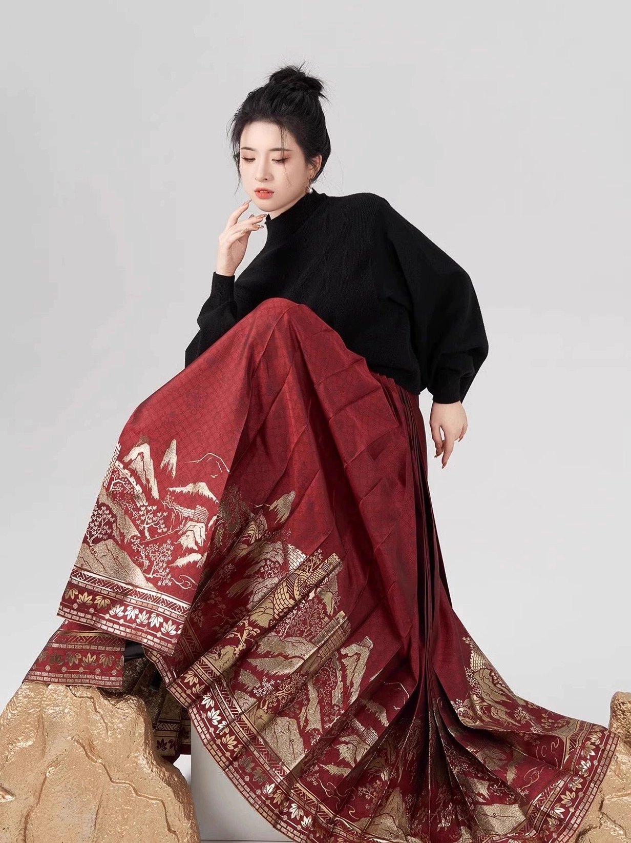 Close view of wine-red Chinese mamian skirt with golden traditional landscape pattern and side tie straps styled with black turtleneck