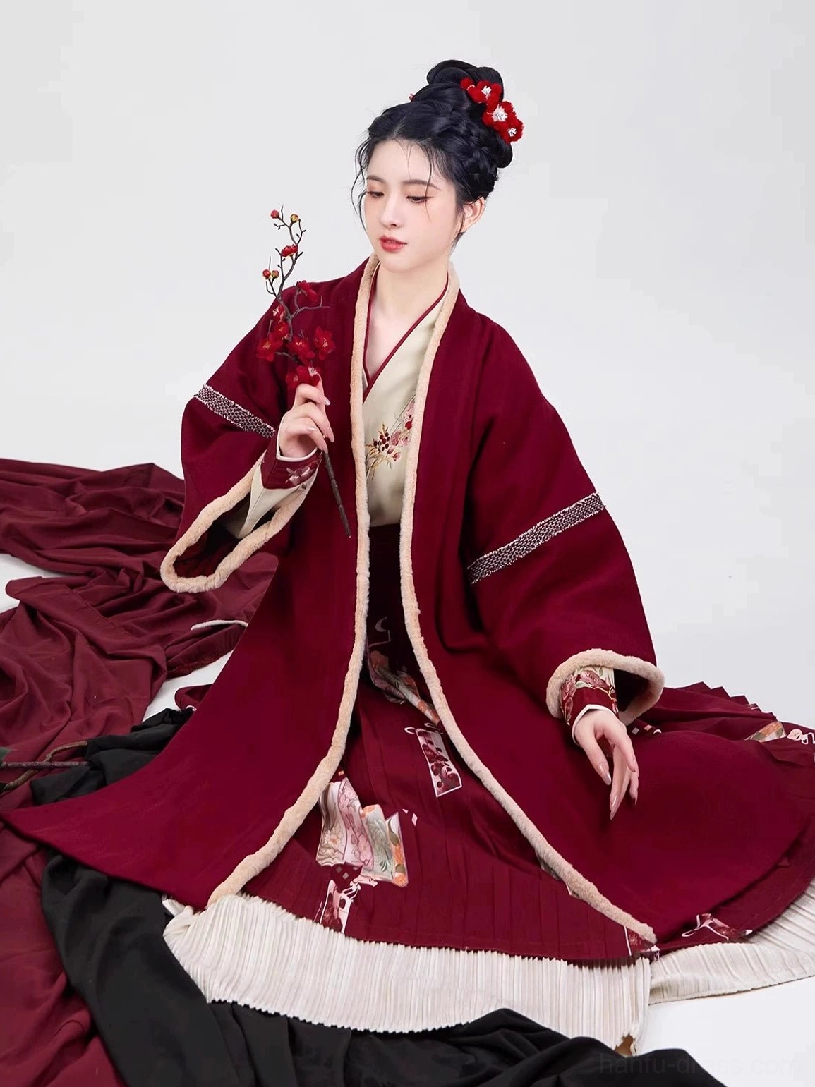 Wine red Song Dynasty modern hanfu outfit shown in a seated view with layered skirt, striped sleeve details, floral embroidery, and plum blossom styling