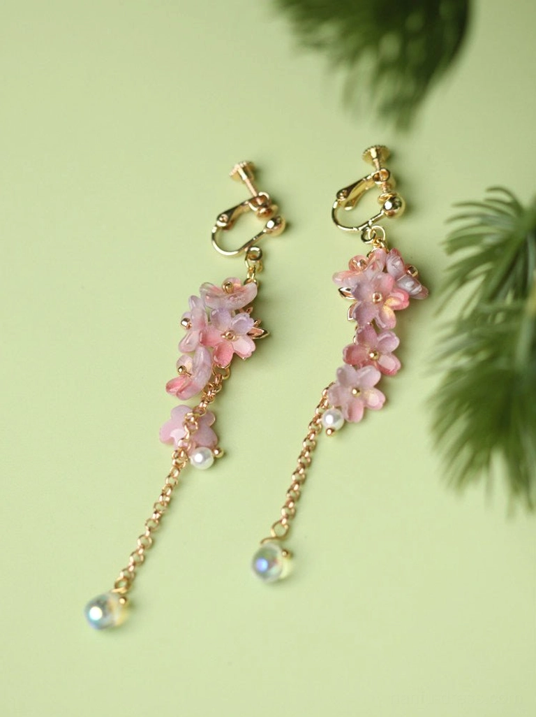 Comfort clip on wisteria flower drop earrings with pink gradient blossoms, pearl details and iridescent teardrop charms on a green background