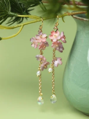 Pink wisteria glazed flower drop earrings with pearl beads, gold tone chains and iridescent teardrop pendants displayed beside a celadon vase