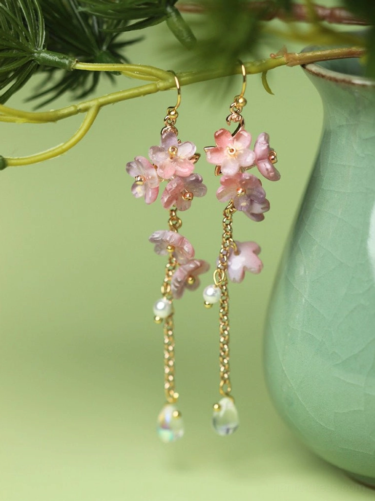 Pink wisteria glazed flower drop earrings with pearl beads, gold tone chains and iridescent teardrop pendants displayed beside a celadon vase