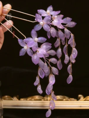 Close-up of a wisteria Hanfu hair pin with lavender purple glass flowers and dangling petal tassels held over a vintage golden decorative tray