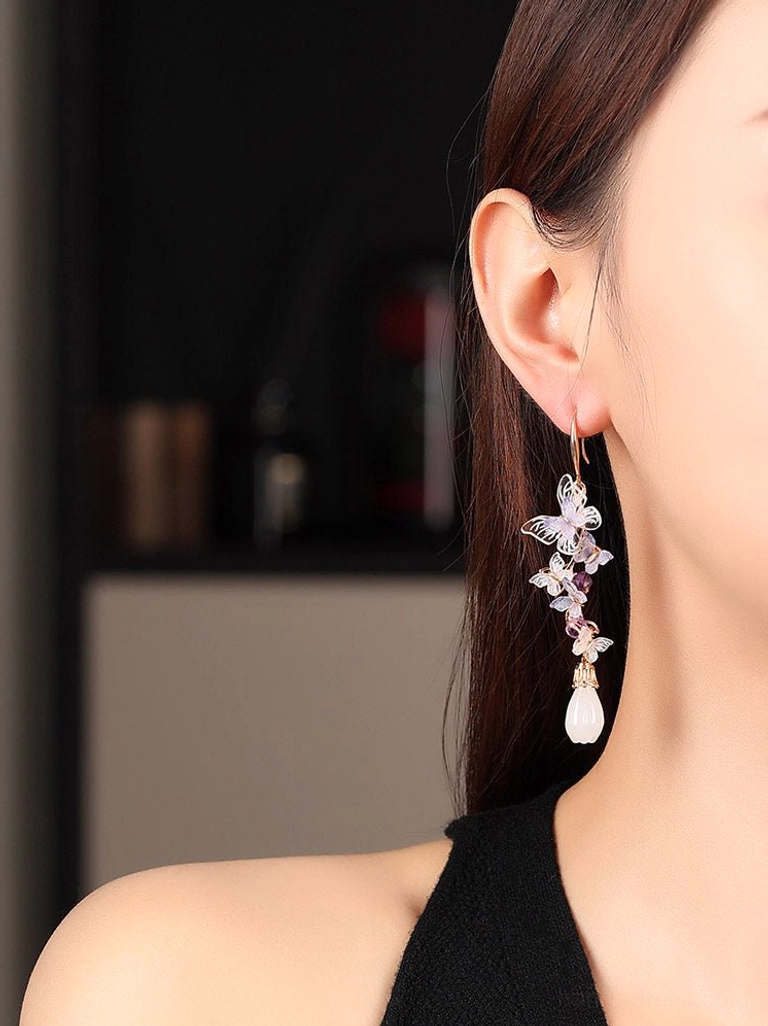 Woman wearing long amethyst butterfly drop earrings with purple bead clusters and white teardrop pendants, shown in side profile